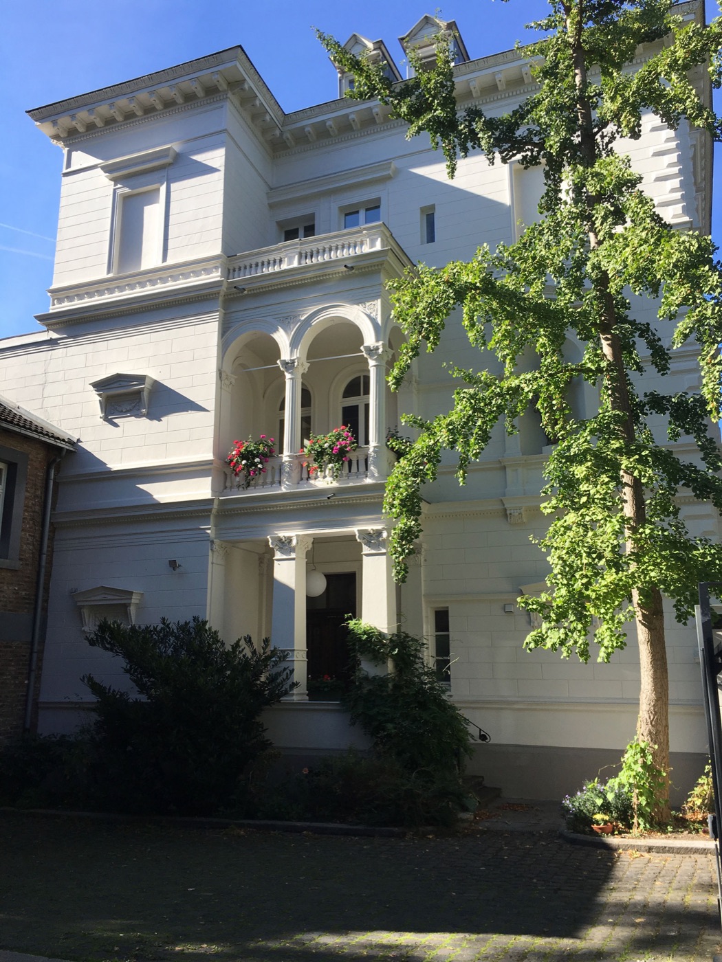 Die weiße Fassade des Hauses Erk mit Säulenbalkon und Blumenkästen